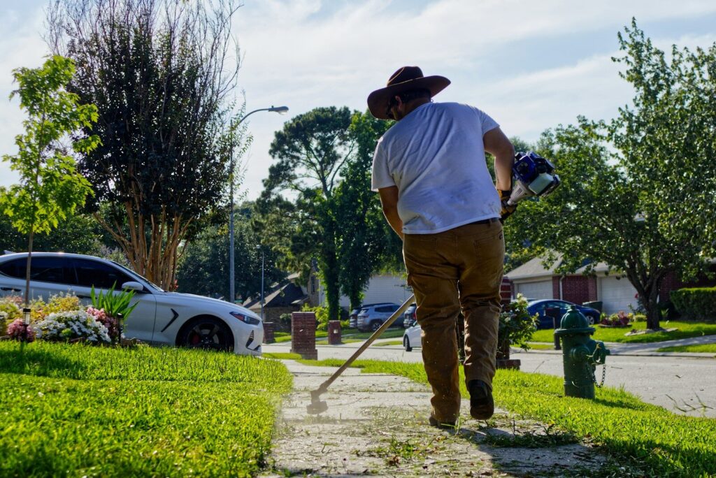 Man trimming weeds on a sunny residential sidewalk