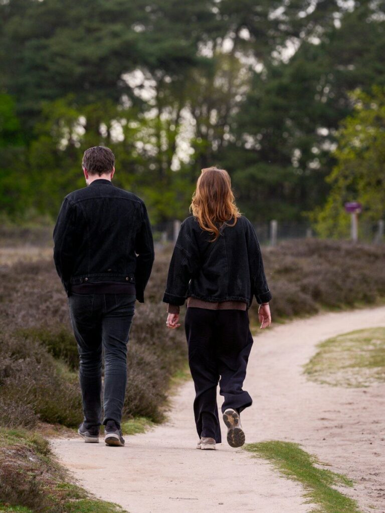 Two people walking on a dirt path through woods