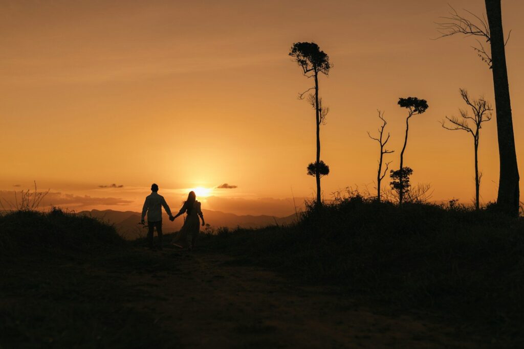 a man and a woman holding hands as the sun sets